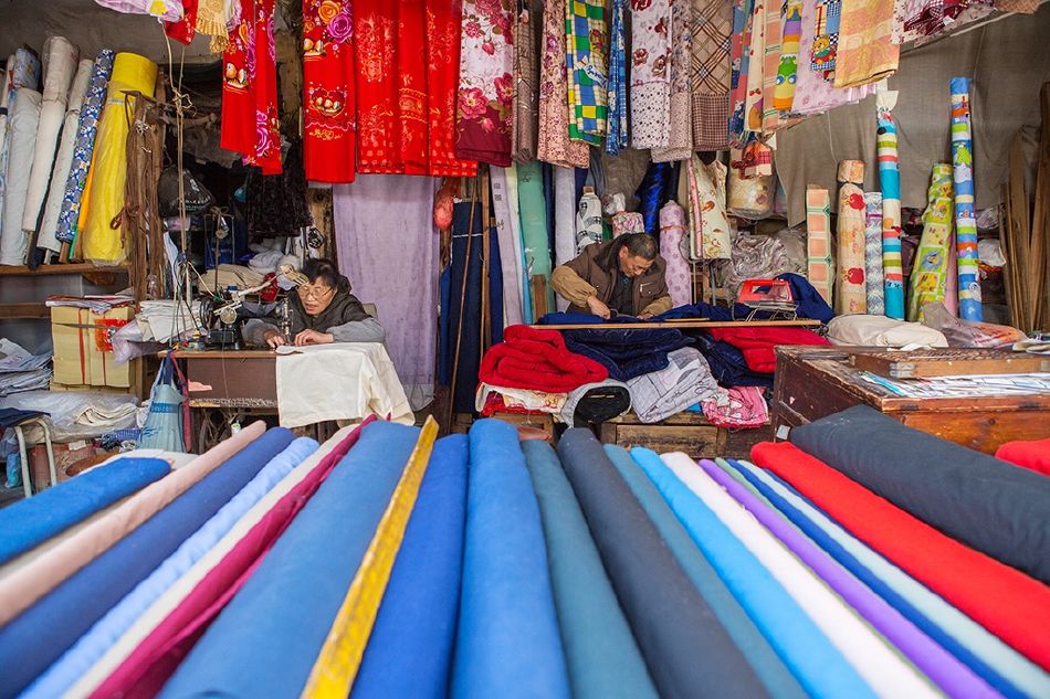 照片描述: 古老式的布店里摆满了五颜六色的布料,老夫妻正忙活着.